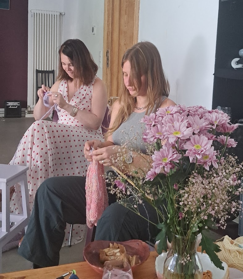 Two people knitting and crocheting together around a table with flowers