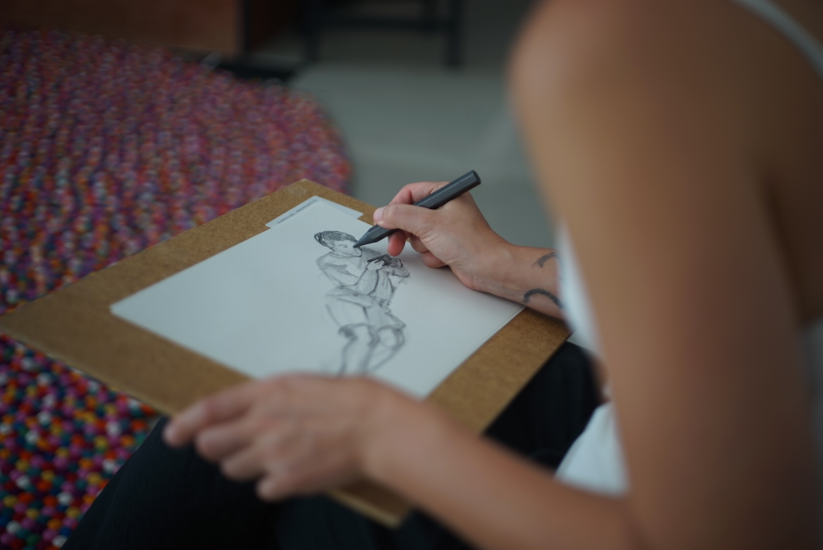 A woman sketches a figure study on a clipboard, seated in the studio