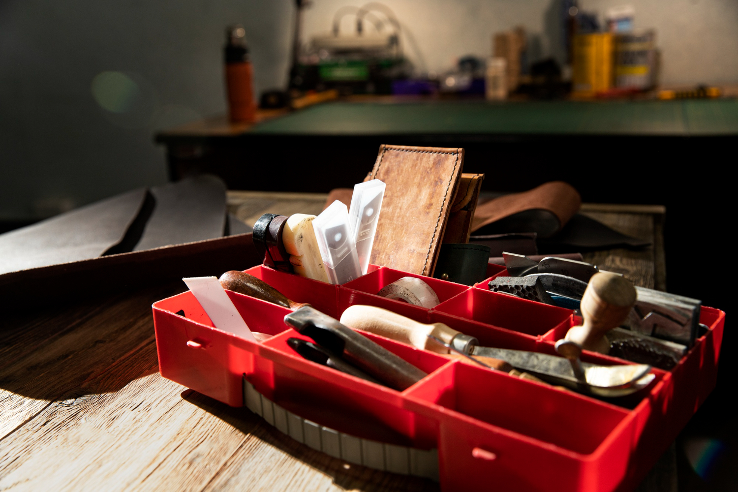 An open toolbox of repair tools and leather pieces on the studio's workbench